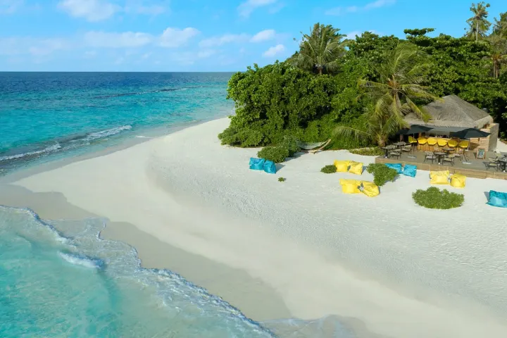 Avani+ Fares Maldives Resort — пляжный бар с креслами на песке в тени пальм