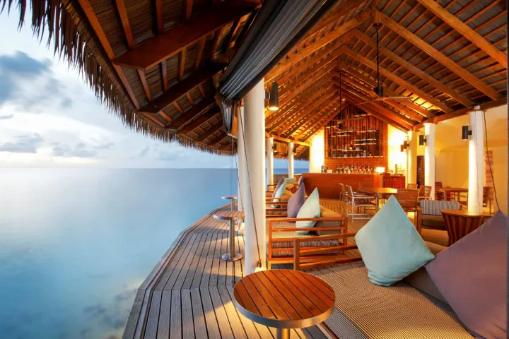 Centara Ras Fushi Resort & Spa Maldives, Мальдивы — бар Centara Ras Fushi Resort & Spa Maldives — лаундж зона с диванами на открытой деревянной террасе у воды