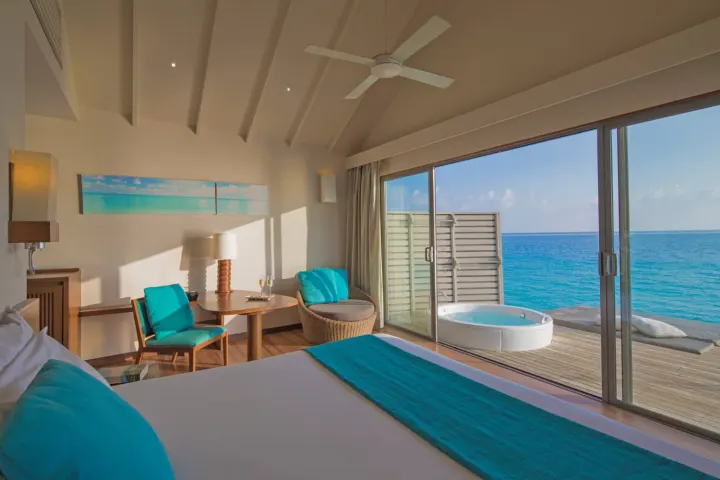 Centara Ras Fushi Resort & Spa Maldives, Мальдивы — интерьер виллы Centara Ras Fushi Resort & Spa Maldives — светлая спальня с большой кроватью и панорамным окном на океан