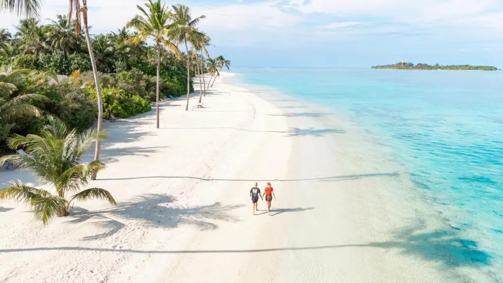 Cocoon Maldives — пара гуляет по широкому белоснежному пляжу