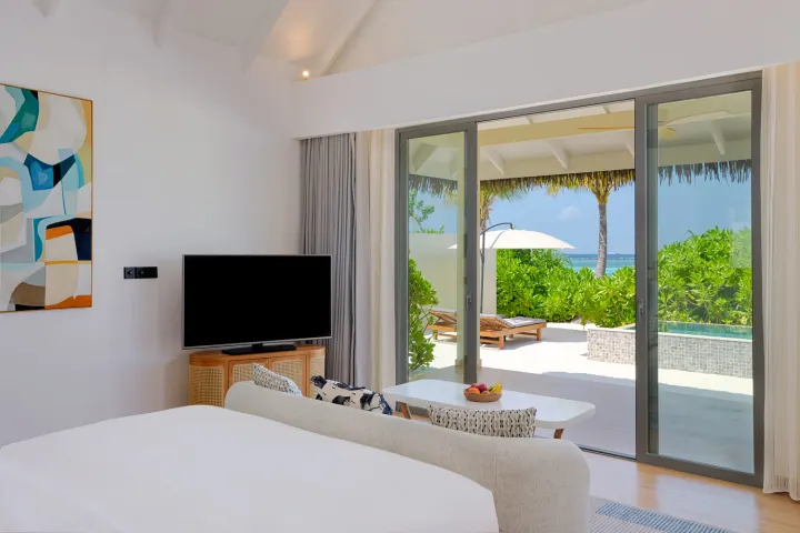 dusitD2 Feydhoo Maldives — современный интерьер спальни с панорамным остеклением и видом на пляж