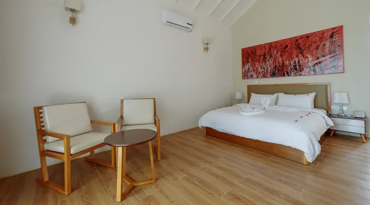 Hondaafushi Island Resort — светлая спальня берегового бунгало с большой кроватью и зоной отдыха