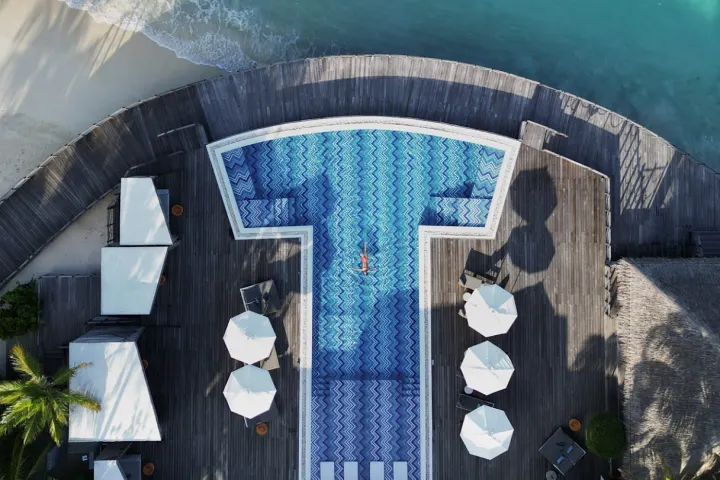JW Marriott Maldives Resort & Spa — панорамный бассейн у кромки пляжа с видом на бескрайний океан и закат