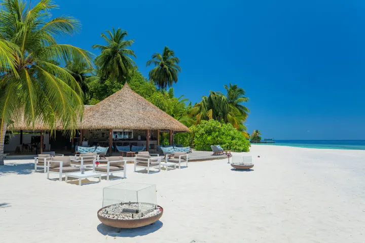Kandolhu Maldives — открытая терраса бара на пляже с соломенной крышей