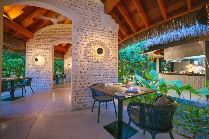 Kandolhu Maldives — столик ресторана с каменными стенами и открытой кухней