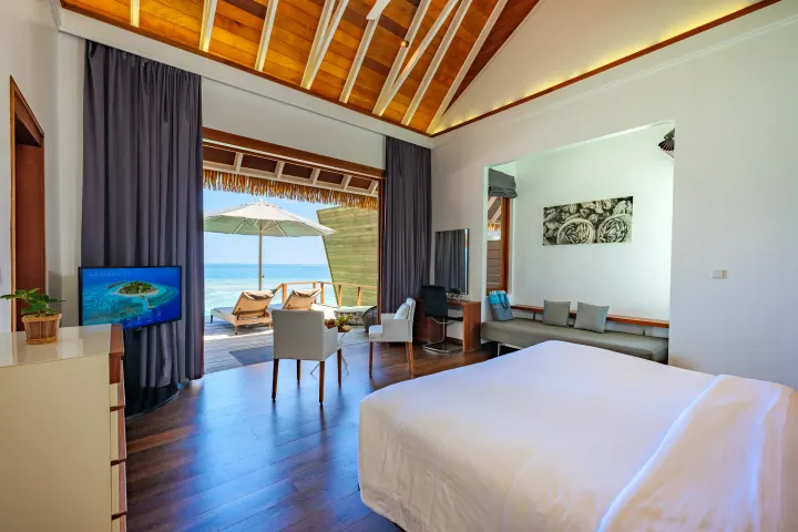 Kandolhu Maldives — просторная спальня водной виллы с телевизором и диваном