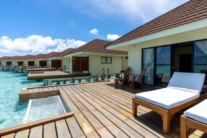 NAKAI Alimatha Resort — интерьер водного бунгало с деревянной отделкой и кроватью