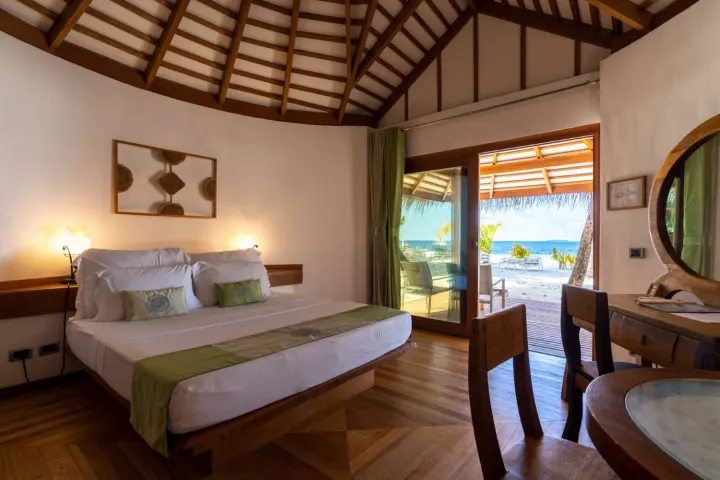 NAKAI Dhiggiri Resort — светлая спальня берегового бунгало в натуральных тонах с видом на пляж