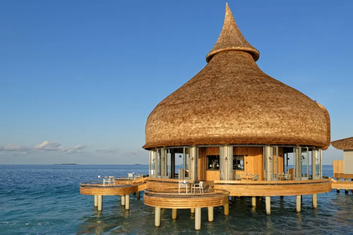 Outrigger Maldives Maafushivaru Resort — ресторан с круглой соломенной крышей над водой