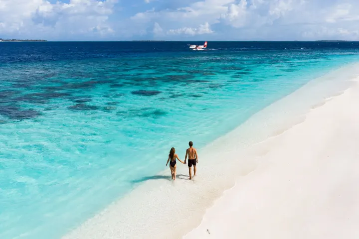 Reethi Faru Resort, Мальдивы — пляж Reethi Faru Resort — пара гуляет по белому песку у лагуны