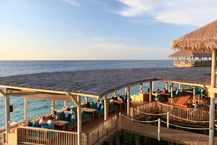 Six Senses Laamu, Мальдивы — ресторан Six Senses Laamu — ресторан с соломенной крышей и мостом над водой вечером