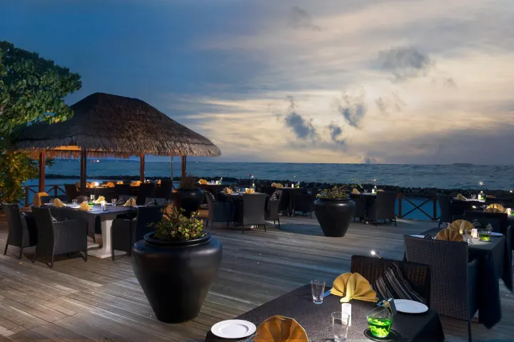 Taj Coral Reef Resort & Spa — ресторан на деревянной террасе у океана на закате