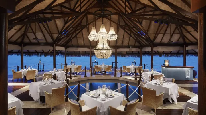 Taj Exotica Resort & Spa, Мальдивы — ресторан Taj Exotica Resort & Spa — ресторан над водой с большой люстрой вечером