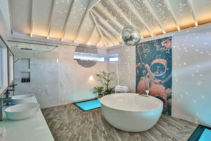 The Standard, Huruvalhi Maldives — просторная ванная комната водной виллы с круглой ванной и диско-шаром