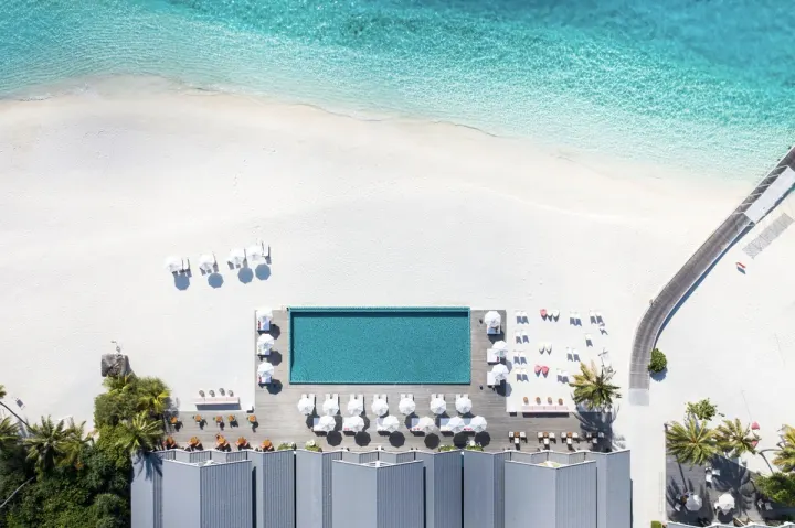 The Standard, Huruvalhi Maldives — главный бассейн курорта у пляжа с яркими шезлонгами и зонтиками